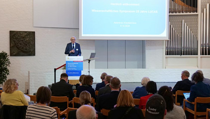 Prof. Dr. Wolfgang von Renteln-Kruse steht am Rednerpult und spricht zum Publikum vor einer Projektionsleinwand bei der Jubiläumsveranstaltung mit Symposium und einer Dankesveranstaltung zum 25-jährige Bestehen der LUCAS Langzeit-Kohortenstudie im Hamburger Albertinen Haus und Kirche am Albertinen Krankenhaus.