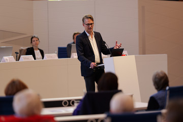 Prof. Dr. Karsten Sydow spricht auf der Bühne zum Publikum im Sitzungssaal beim 2. Norderstedter Herz- und Gefäßtag mit dem Albertinen Herz- und Gefäßzentrum Hamburg im Norderstedter Rathaus