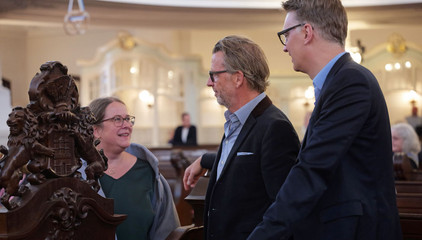 Drei Konzertgäste unterhalten sich im Kirchensaal beim 10. Herzbrücke-Benefizkonzert im Hamburger „Michel“ der Albertinen-Stiftung.