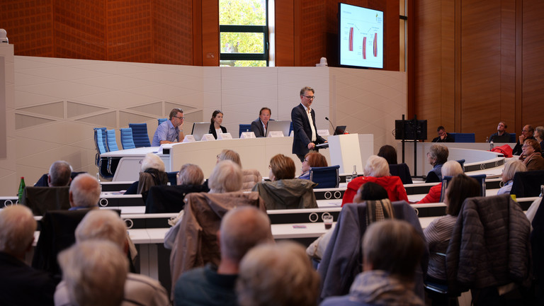Blick über die Zuschauerreihen aufs Podium mit dem Chefarzt der Kardiologie am Standort Hamburg-Schnelsen Prof. Karsten Sydow beim 2. Norderstedter Herz- und Gefäßtag mit dem Albertinen Herz- und Gefäßzentrum Hamburg im Norderstedter Rathaus