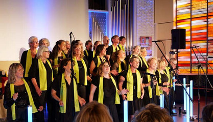 Der Albertinen Mitarbeitenden Gospelchor steht beim Singen auf der Bühne mit farbigen Leuchtelementen, einem Kirchenfenster und einem Lautsprecher in der festlich beleuchteten Kirche am Albertinen Krankenhaus in Hamburg.