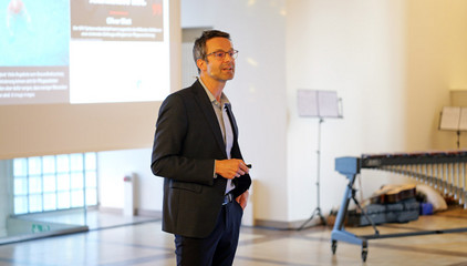 Prof. Dr. Michael Denkinger spricht zum Publikum vor einer Projektsleinwand beim Einführungssymposium „Die Zukunft ist alt!“ von Priv.-Doz. Dr. Gödel, Chefarzt der Klinik für Geriatrie im Albertinen Zentrum für Altersmedizin im Albertinen Krankenhaus in Hamburg.