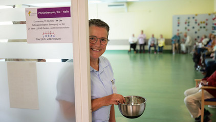 Eine Mitarbeiterin in Funktionskleidung steht lächelnd in der Eingangstür zum großen Saal bei der Jubiläumsveranstaltung mit Symposium und einer Dankesveranstaltung zum 25-jährige Bestehen der LUCAS Langzeit-Kohortenstudie im Hamburger Albertinen Haus und Kirche am Albertinen Krankenhaus.