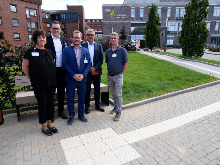 Ein Team mit dem Vorsitzenden der Konzerngeschäftsführung, Matthias Scheller, und Krankenhausgeschäftsführer Christian Rilz steht vor einer Ruhebank der neuen Zuwegung des Albertinen Krankenhauses in Hamburg-Schnelsen