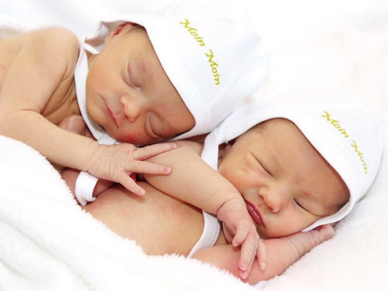 Zwei Neugeborene Babys liegen aneinandergekuschelt mkit weißenb Mützchen auf einer Decke Zwei Neugeborene Babys liegen aneinandergekuschelt mkit weißenb Mützchen auf einer Decke