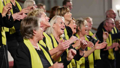 In den Reihen des Albertinen Mitarbeitenden Gospelchors in festlicher Kleidung wird geklatscht und gesungen beim 10. Herzbrücke-Benefizkonzert im Hamburger „Michel“ der Albertinen-Stiftung.
