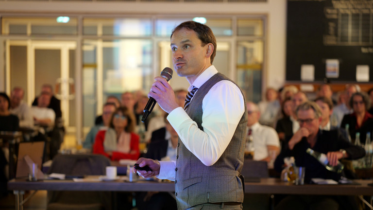 Priv.-Doz. Dr. Gödel, Chefarzt der Klinik für Geriatrie im Albertinen Zentrum für Altersmedizin im Albertinen Krankenhaus in Hamburg, spricht mit einem Mikrofon in der Hand zum Publikum bei seinem Einführungssymposium „Die Zukunft ist alt!“.