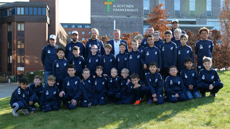 Spieler der F-Jugend Fußball TUS Germania Schnelsen in gesponsorten Trainingsanzügen mit Trainern und dem Personaldirektor Sören Jonasson vom Albertinen Krankenhaus vor dem Krankenhausgebäude