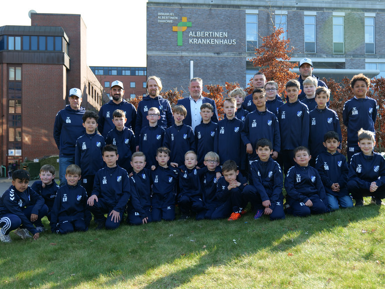 Spieler der F-Jugend Fußball TUS Germania Schnelsen in gesponsorten Trainingsanzügen mit Trainern und dem Personaldirektor Sören Jonasson vom Albertinen Krankenhaus vor dem Krankenhausgebäude