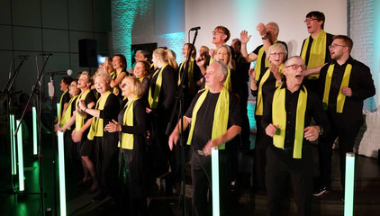 Der Albertinen Mitarbeitenden Gospelchor steht beim Singen auf der Bühne vor bunten Leuchtstäben in der festlich beleuchteten Kirche am Albertinen Krankenhaus in Hamburg. 