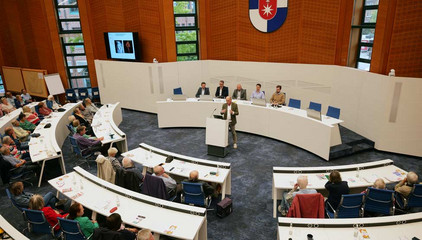 Blick in den Großen Sitzungssaal mit dem Wappen Norderstedts, zahlreichen Zuhörenden, den Vortragenden und Redner am Pult beim 3. Norderstedter Herz- und Gefäßtag im Rathaus Norderstedt.