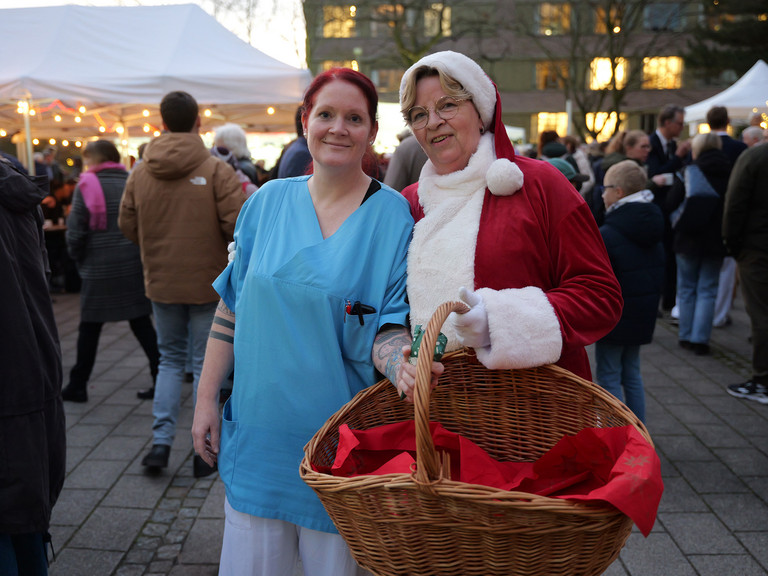 Pflegekraft und Weihnachtsfrau der Immanuel Albertinen Diakonie stehen lächelnd am Abend zusammen Pflegekraft und Weihnachtsfrau der Immanuel Albertinen Diakonie stehen lächelnd am Abend zusammen
