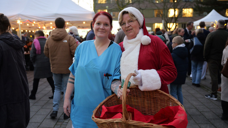 Pflegekraft und Weihnachtsfrau der Immanuel Albertinen Diakonie stehen lächelnd am Abend zusammen Pflegekraft und Weihnachtsfrau der Immanuel Albertinen Diakonie stehen lächelnd am Abend zusammen