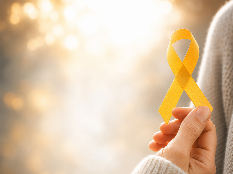 Hand hält eine gelbe Awareness-Schleife als Symbol für Suizidprävention vor einem warmen, hellen Hintergrund.